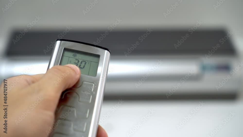 man's hand with remote control is aimed at air conditioner. By moving your finger and pressing button, numbers on display change, raising temperature and cooling it. Air conditioning and heating. man's hand with remote control is aimed at air conditioner. By moving your finger and pressing button, numbers on display change, raising temperature and cooling it. Air conditioning and heating.
