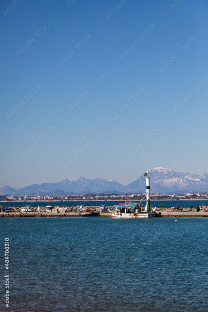 pier with a beautiful white lighthouse and a pier with many boats and yachts on the background of the blue sea