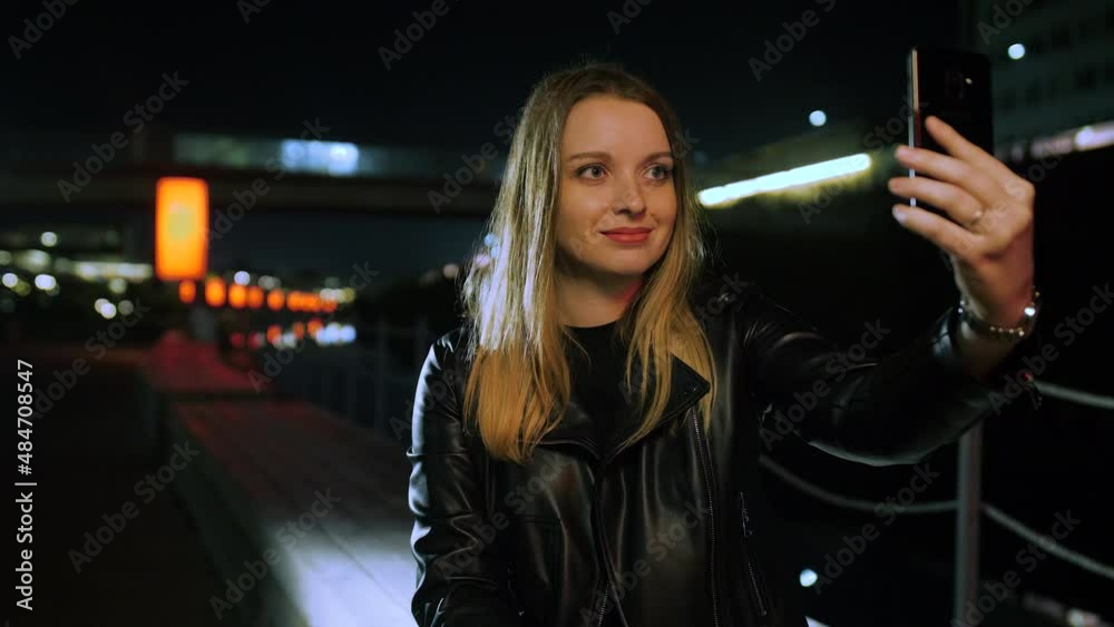 Young woman sitting on a red-lit street taking a selfie on a smartphone Young woman sitting on a red-lit street taking a selfie on a smartphone