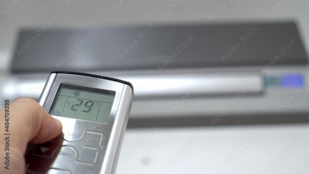 man's hand with remote control is aimed at air conditioner. By moving your finger and pressing button, numbers on display change, raising temperature and cooling it. Air conditioning and heating. man's hand with remote control is aimed at air conditioner. By moving your finger and pressing button, numbers on display change, raising temperature and cooling it. Air conditioning and heating.
