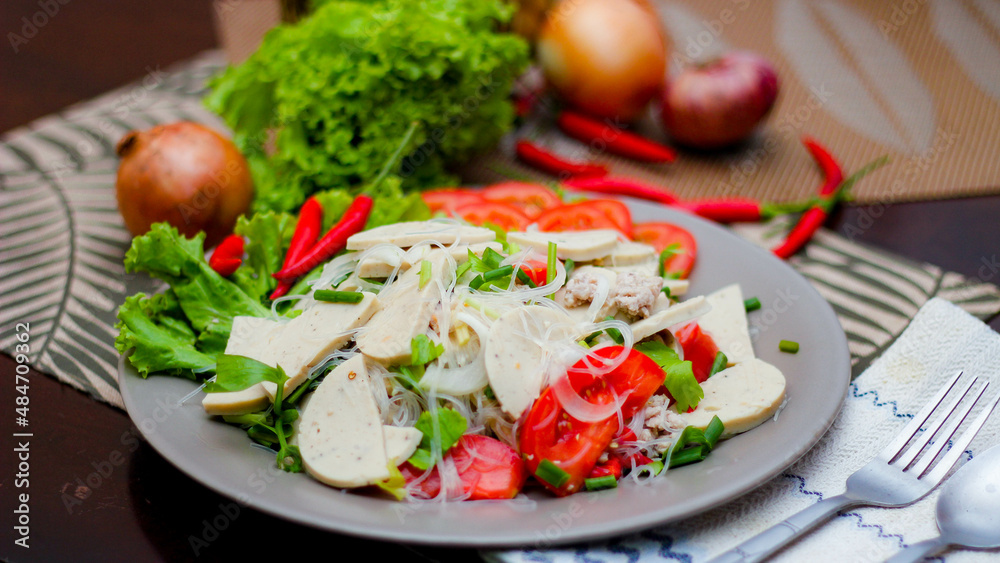 Spicy Glass Noodle Salad with Vietnamese Sausage  served in a gray plate Put on a wooden table and various vegetables.