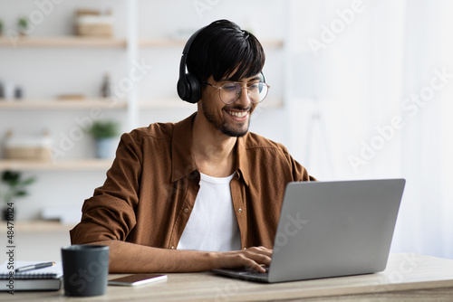 Smiling indian guy attending webinar, typing on laptop keyboard