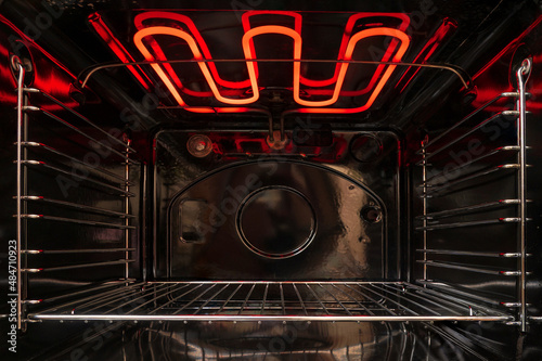 Looking inside the black empty kitchen oven. There is a lattice shelf and a red hot heating element. Background.