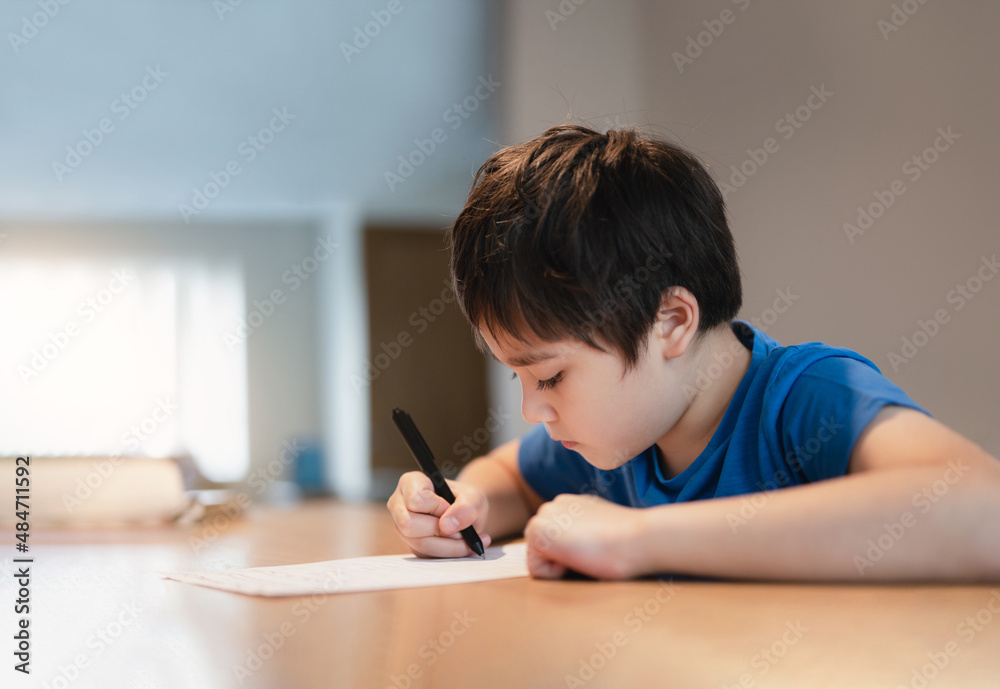 School kid using black pen drawing or writing the letter on paper, Young boy doing homework, Child with pen writing notes in paper sheet during the lesson.Cute pupil doing test, Homeschooling concept School kid using black pen drawing or writing the letter on paper, Young boy doing homework, Child with pen writing notes in paper sheet during the lesson.Cute pupil doing test, Homeschooling concept