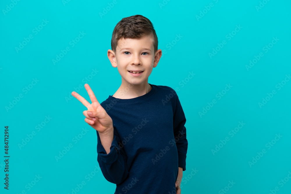 Little kid boy isolated on blue background smiling and showing victory sign Little kid boy isolated on blue background smiling and showing victory sign