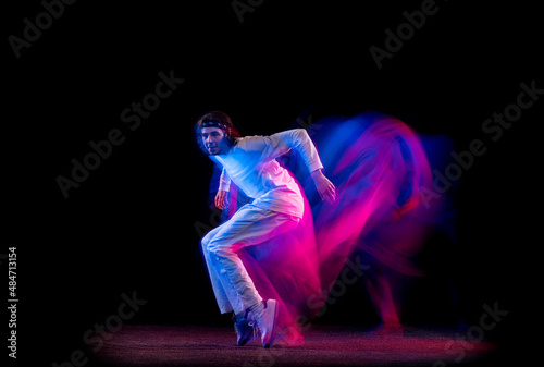 Street style. Male hip-hop dancer dancing isolated on dark background in mixed neon light. Youth culture, hip-hop, movement, style and fashion, action.