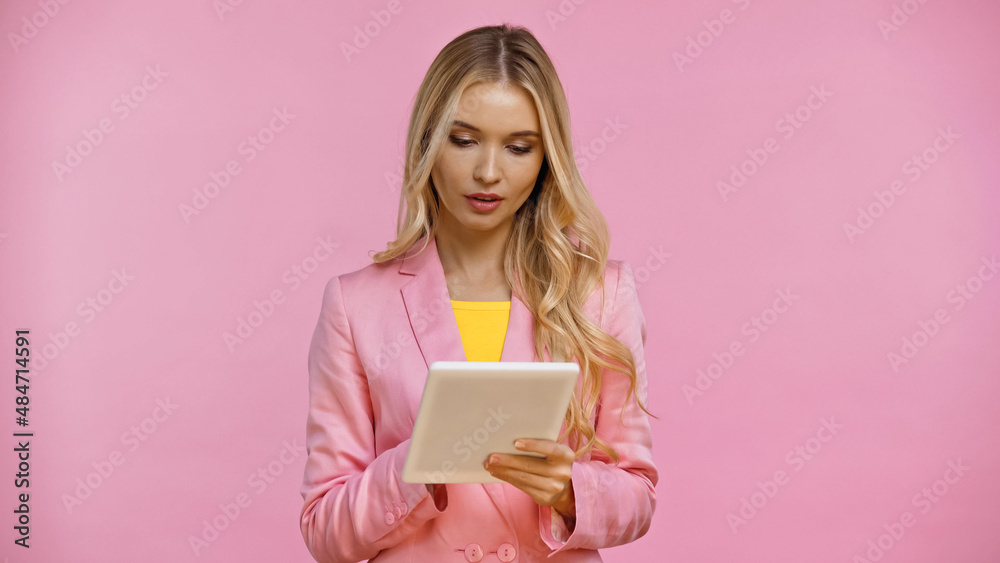 Blonde woman in jacket using digital tablet isolated on pink.
