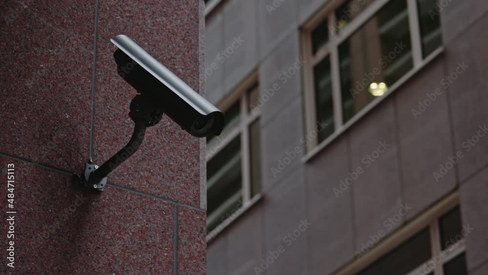 Security camera moving panning and tilting recording what's happening outside a building. Motorized CCTV surveillance concept. Security camera moving panning and tilting recording what's happening outside a building. Motorized CCTV surveillance concept.