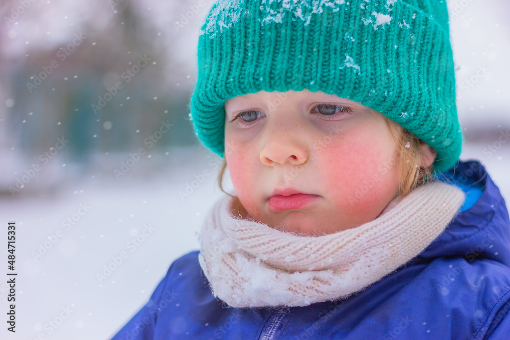 portrait of a little boy in a green knitted hat and white scarf on a snowy street. winter holidays, outdoor activities in the snow, childhood. portrait of a little boy in a green knitted hat and white scarf on a snowy street. winter holidays, outdoor activities in the snow, childhood.