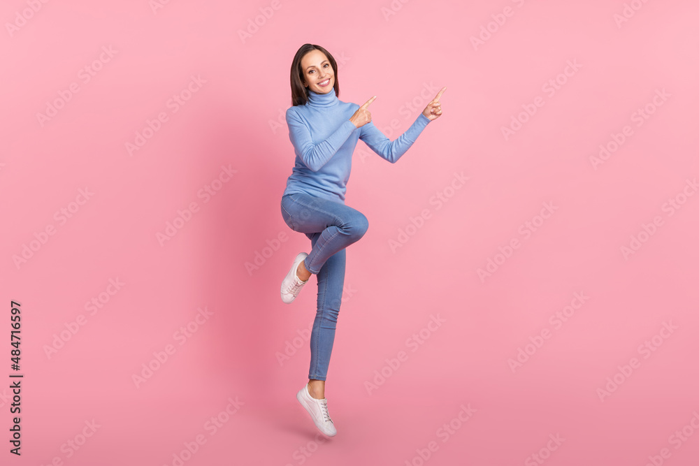 Photo of cheerful lady jump direct finger empty space wear blue turtleneck isolated pink color background Photo of cheerful lady jump direct finger empty space wear blue turtleneck isolated pink color background