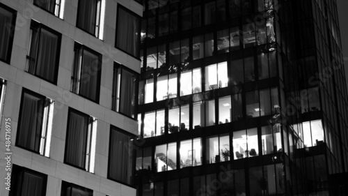 Amazing night cityscape. Office building at night, building facade with glass and lights. View with illuminated modern skyscraper. Scenic glowing windows of skyscrapers at evening. Black and white.