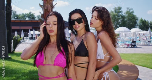 Adorable young women in sunglasses and stylish swimwear standing closely to each other near swimming pool. Concept of people, summer and relaxation.