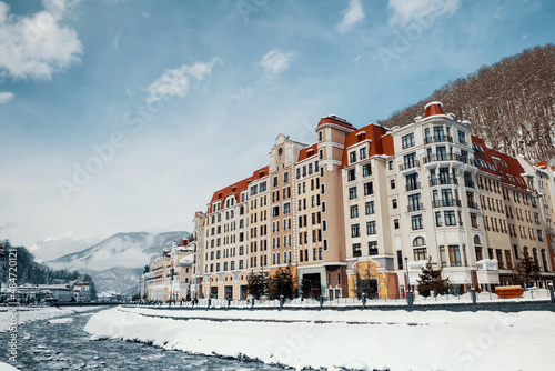 Winter hotel building at ski resort near by river. Beautiful snow landscape with a blue sky.