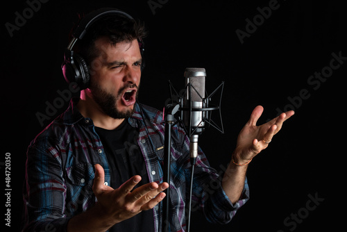 Hombre cantor grabando su voz con microfono de condensador y auriculares