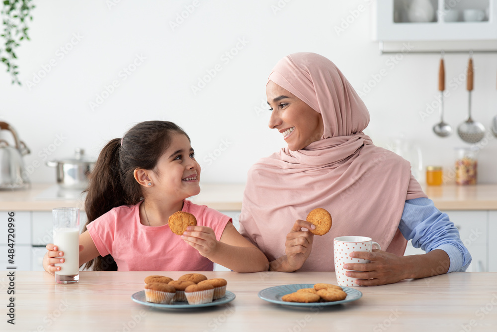 Happy Little Girl And Her Islamic Mom Having Snacks In Kitchen Together Happy Little Girl And Her Islamic Mom Having Snacks In Kitchen Together