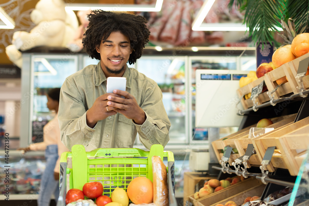 African American Man Doing Grocery Shopping Using Smartphone In Supermarket
