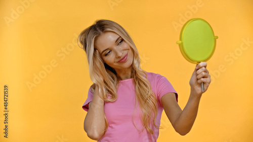 Pretty blonde woman smiling while holding mirror isolated on yellow. © LIGHTFIELD STUDIOS