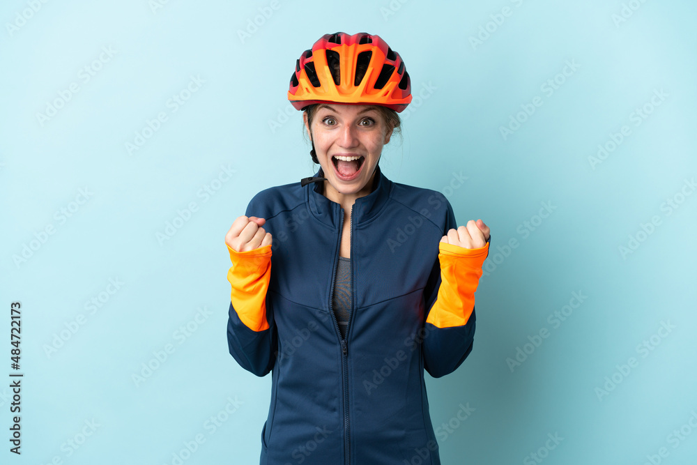 Young cyclist woman isolated on blue background celebrating a victory in winner position - obrazy, fototapety, plakaty 