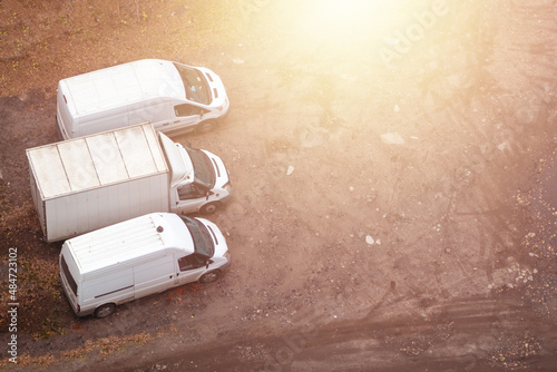Top view of three white truck vans parked on warehouse area. Copy space. Yellow glow.