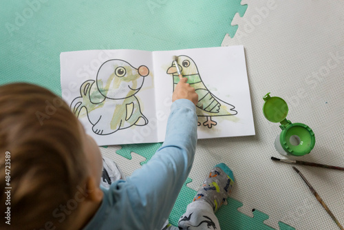 Boy coloring with brush a pigeon in water book photo