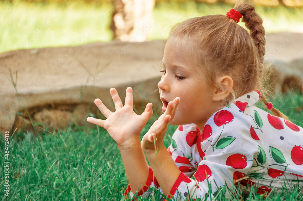 A beautiful little girl is lying on the green grass and resting. The girl plays carefree in nature. The concept of rest and a happy life A beautiful little girl is lying on the green grass and resting. The girl plays carefree in nature. The concept of rest and a happy life
