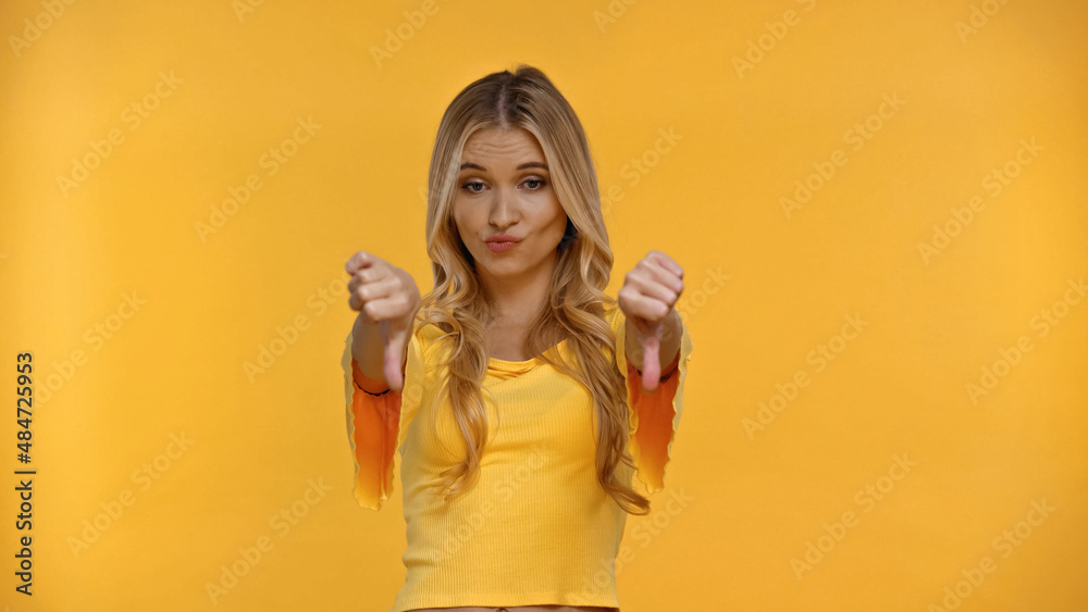 Offended blonde woman showing thumbs up isolated on yellow. Offended blonde woman showing thumbs up isolated on yellow.