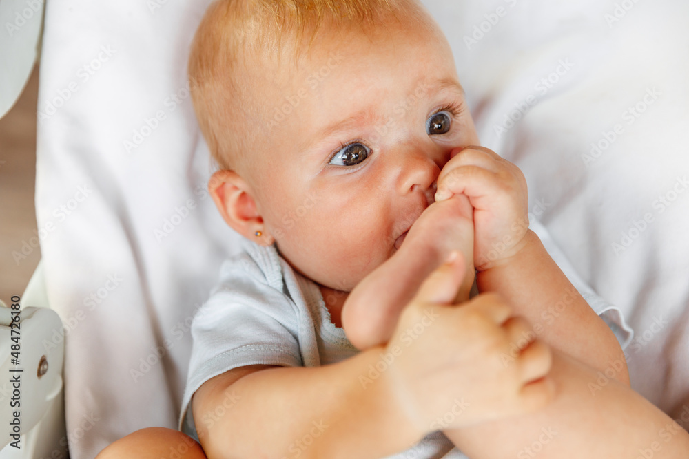 Cute little newborn girl with funny face sucking foot toe on white background. Infant baby resting playing lying down on feeding chair at home. Motherhood happy child concept Cute little newborn girl with funny face sucking foot toe on white background. Infant baby resting playing lying down on feeding chair at home. Motherhood happy child concept