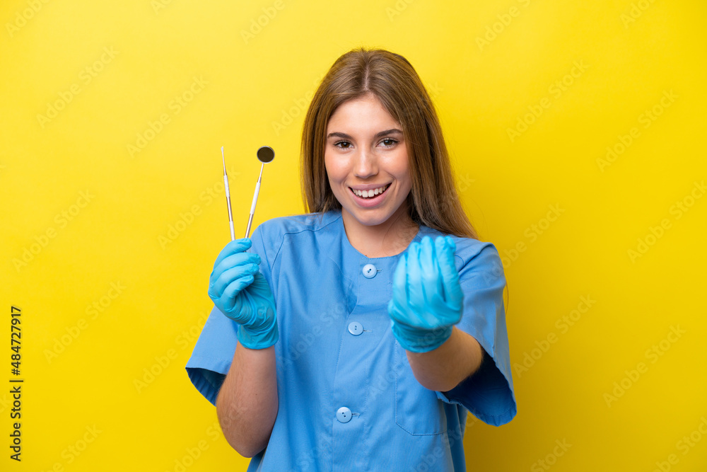 Dentist caucasian woman holding tools isolated on yellow background making money gesture Dentist caucasian woman holding tools isolated on yellow background making money gesture