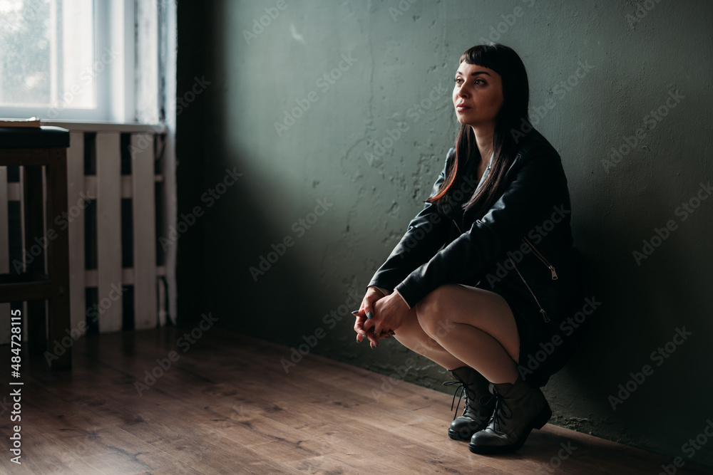 Portrait of a lonely sad woman in black clothes against a dark wall. The concept of loneliness, psychological trauma, stress.