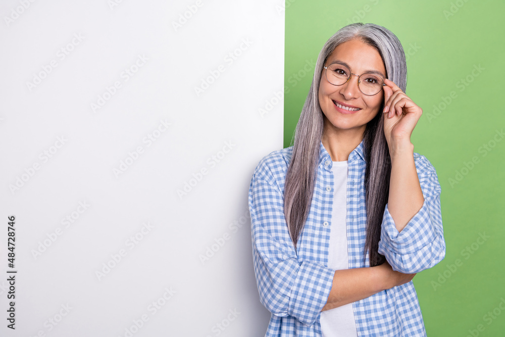 Photo of optimistic aged grey hairdo lady near ad wear spectacles checkered shirt isolated on green color background Photo of optimistic aged grey hairdo lady near ad wear spectacles checkered shirt isolated on green color background