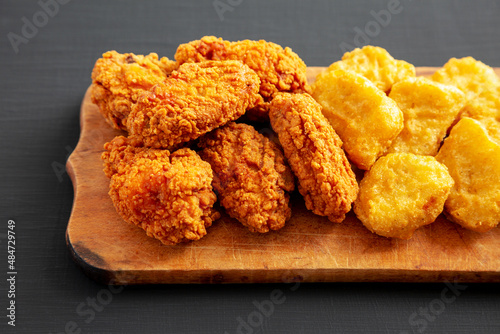Homemade Crispy Fried Chicken Wings and Nuggets on a rustic wooden board on a black background, side view.
