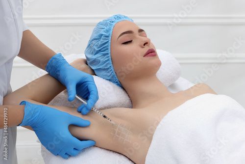 Cosmetologist injecting young woman's armpit in clinic. Treatment of hyperhidrosis