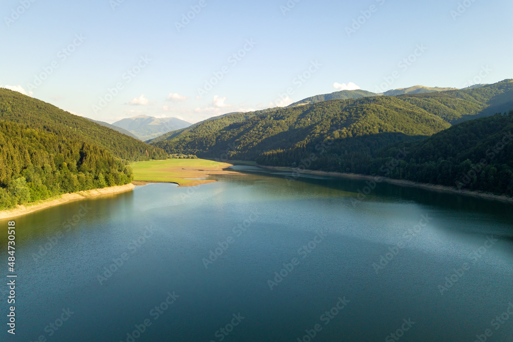 Aerial view of big lake with clear blue water between high mountain hills covered with dense evergreen forest