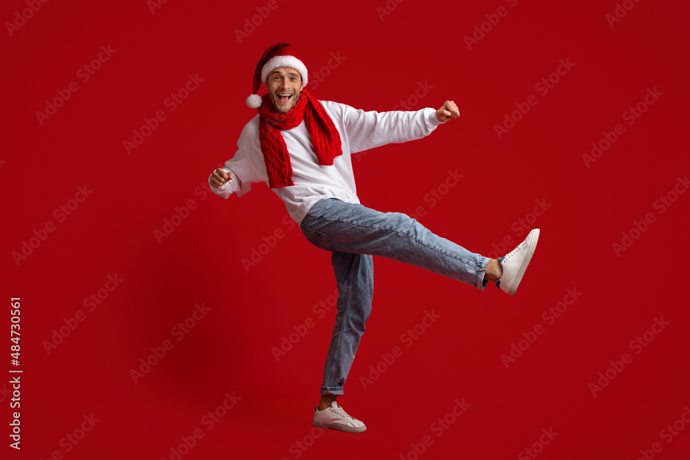 Cheerful Young Man Wearing Santa Hat And Red Scarf Dancing In Studio