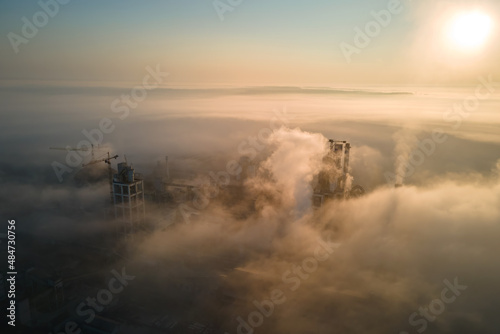 Aerial view of cement factory with high concrete plant structure and tower crane at industrial production site on foggy morning. Manufacture and global industry concept