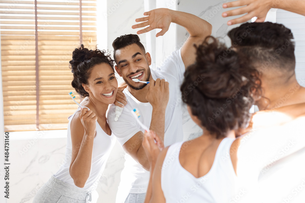 Fototapeta premium Morning Hygiene. Joyful Middle Eastern Couple Brushing Teeth And Dancing In Bathroom