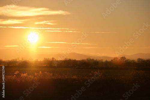 Beautiful evening panoramic landscape with bright setting sun over distant mountain peaks and asphalt road in front at sunset