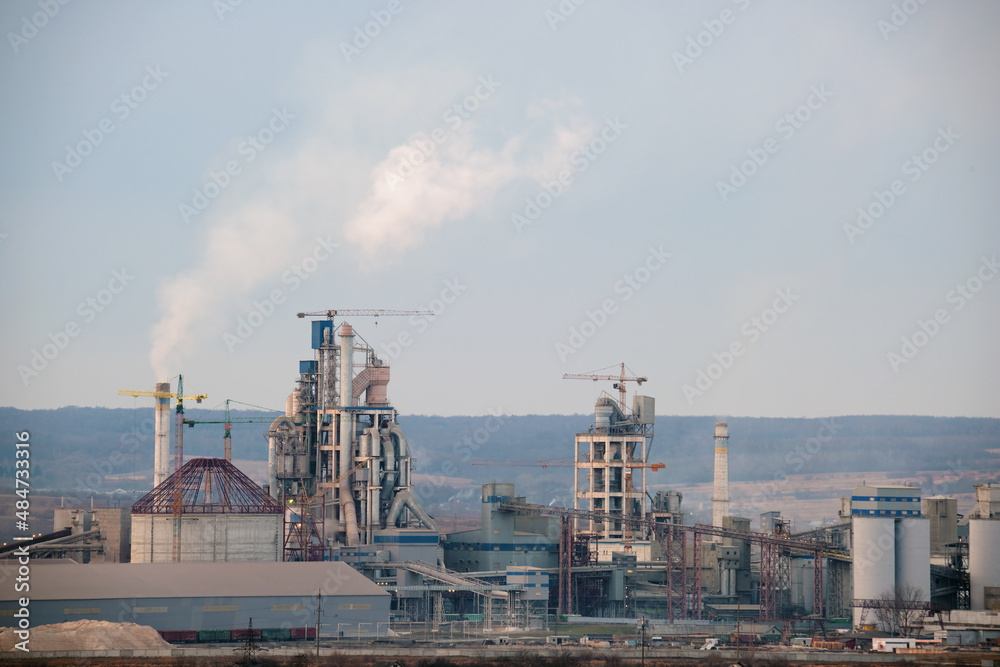 Cement plant with high factory structure and tower cranes at industrial production area. Manufacture, global industry and air pollution concept
