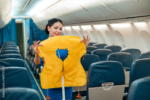 Smiling woman stewardess standing in aircraft passenger salon and holding yellow safety vest