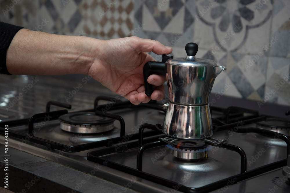 Mano che mette la caffettiera sul fuoco acceso per il caffè, cucina familiare Mano che mette la caffettiera sul fuoco acceso per il caffè, cucina familiare