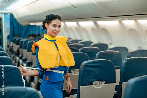 Woman flight attendant or air hostess wearing safety vest while standing in aircraft passenger cabin
