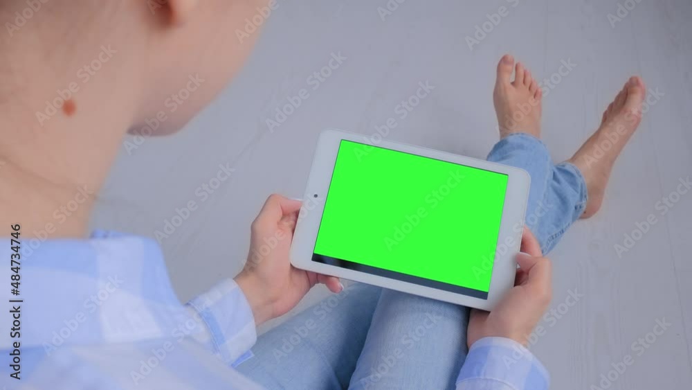 Woman sitting on floor and looking at white tablet computer device with blank green display. Mock up, entertainment, copyspace, freelance, template, leisure time, green screen, technology concept