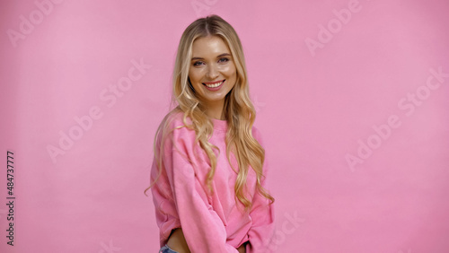 Happy blonde woman in sweatshirt looking at camera isolated on pink.