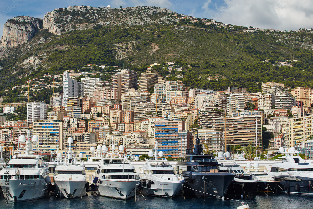 Monaco, Monte-Carlo, a lot of large motor yachts are parked side by side in the port, with huge fenders between them to avoid collision at sunny day, mooring ropes go into the azure water