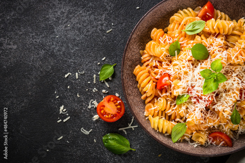 Traditional Italian pasta with tomato sauce, basil and parmesan on black table. Fusilli pasta with tomato sauce arrabbiata. Top view.
