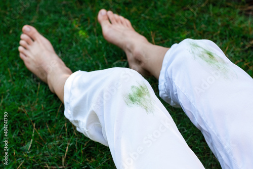 Barefoot girl sitting dirty stain of grass on white pants on a background of green field. top view. outodors photo