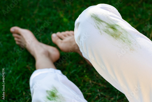 Barefoot girl sitting dirty stain of grass on white pants on a background of green field. top view. outodors photo
