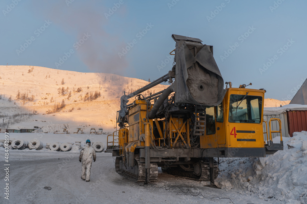 A mechanic walks past a drilling rig. The action takes place at a gold mining site.