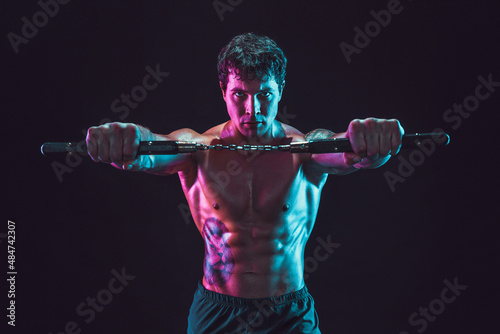 Portrait of muscular man who holds nunchaku while isolated on black background. Sport concept photo