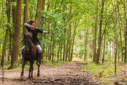 beautiful woman with long hair woman on a horse shooting a bow on the forest path